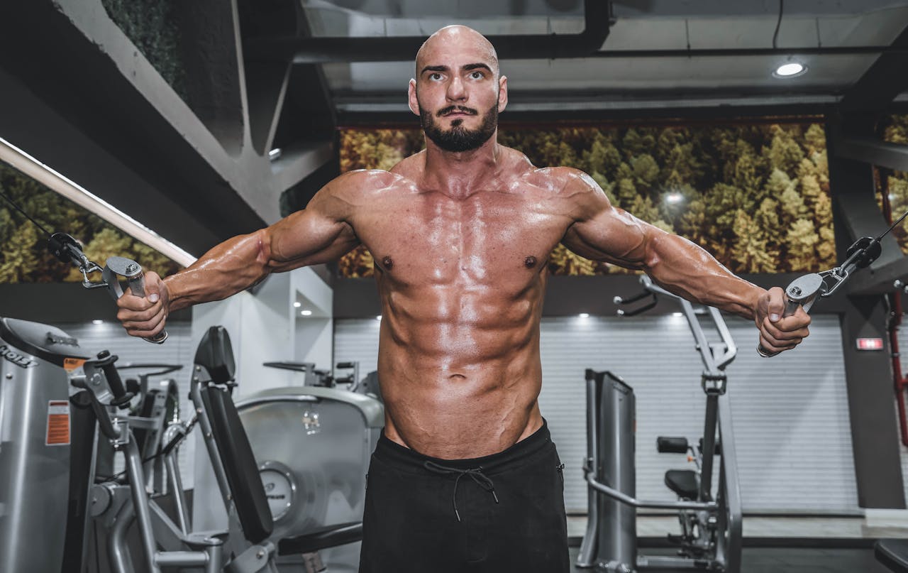Strong bald man exercising shirtless in a gym using cable crossover equipment to enhance fitness and strength.